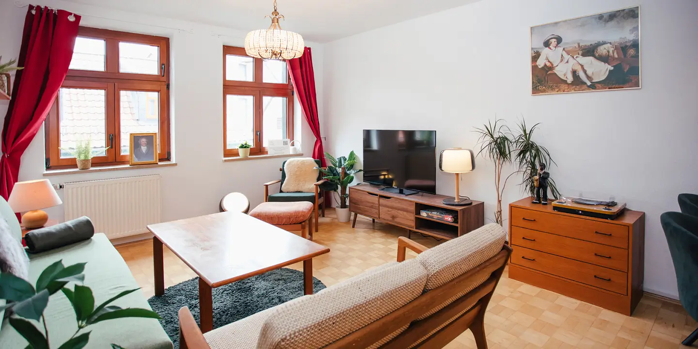 Wohnzimmer der Goethe-Suite in Wernigerode mit Smart-TV, Retro-Möbeln, Goethe-Bild und lichtdurchfluteter Fensterfront